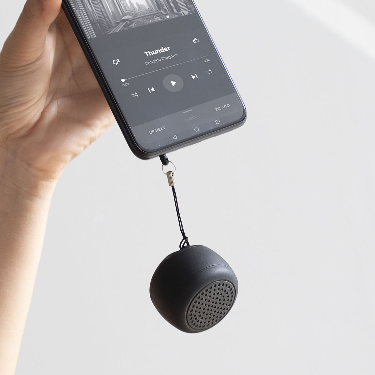 Mano che tiene un telefono con musica, collegato a un piccolo altoparlante nero.