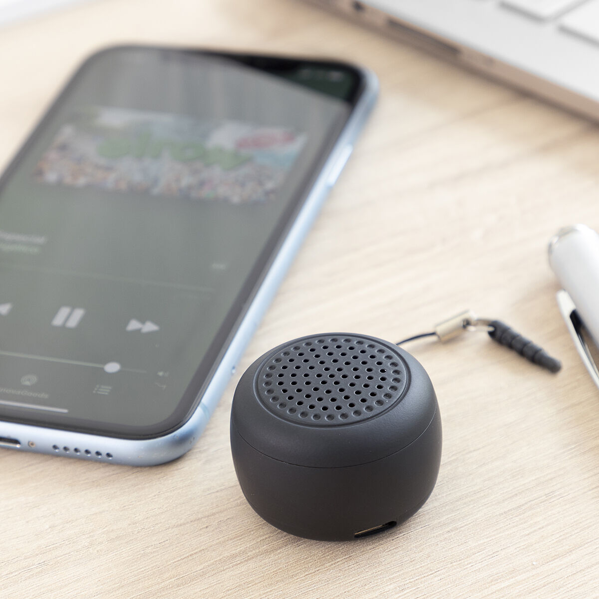 Piccolo altoparlante nero accanto a un telefono che riproduce musica su una superficie di legno.
