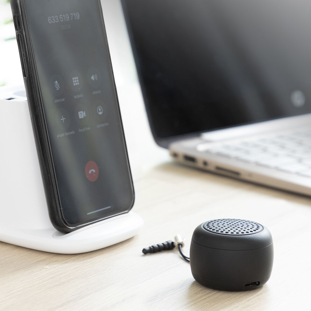 Piccolo altoparlante nero accanto a un telefono su un supporto. Un laptop sullo sfondo.