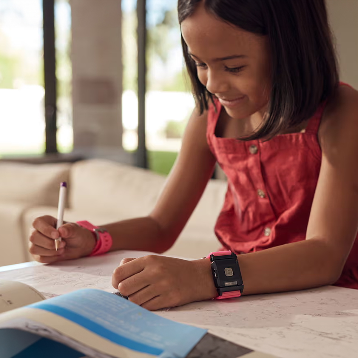 Ein Mädchen schreibt in ein Buch. Sie trägt eine Uhr und ein Armband. Auf dem Tisch liegt ein Buch.