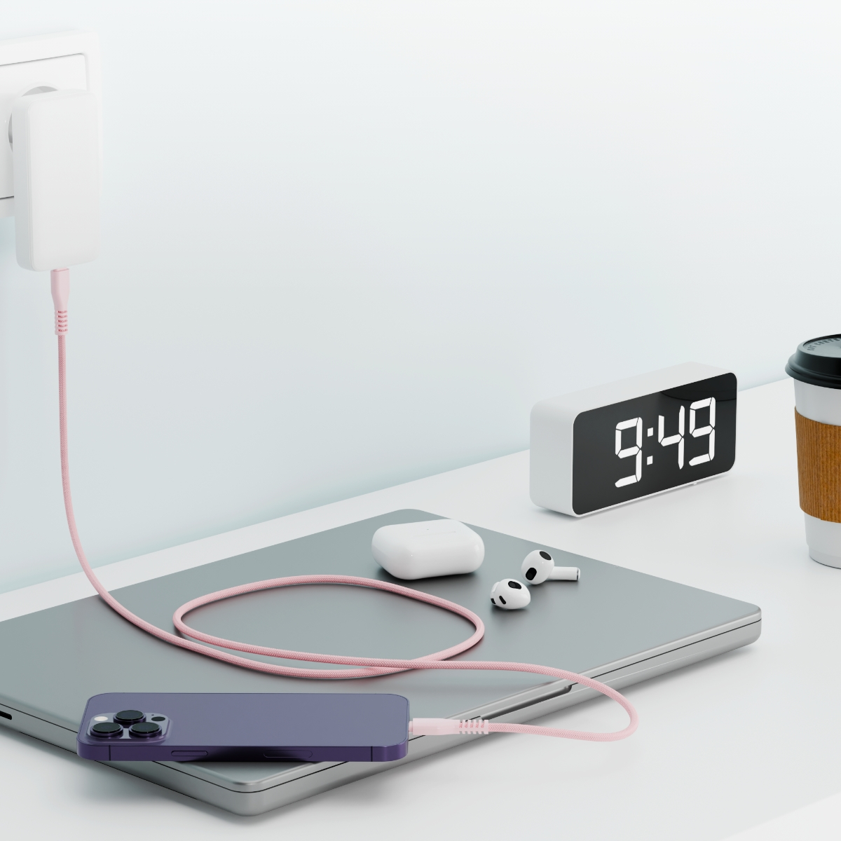 Telefon ładujący się na biurku obok zegara, słuchawek i filiżanki kawy.