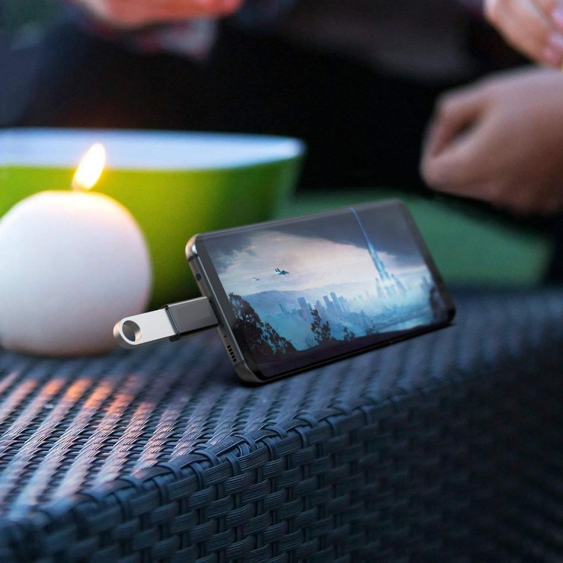 Ein Telefon, das mit einem USB-Laufwerk verbunden ist. Das Telefon zeigt ein Landschaftsbild an. Eine Kerze und eine Schüssel sind im Hintergrund.