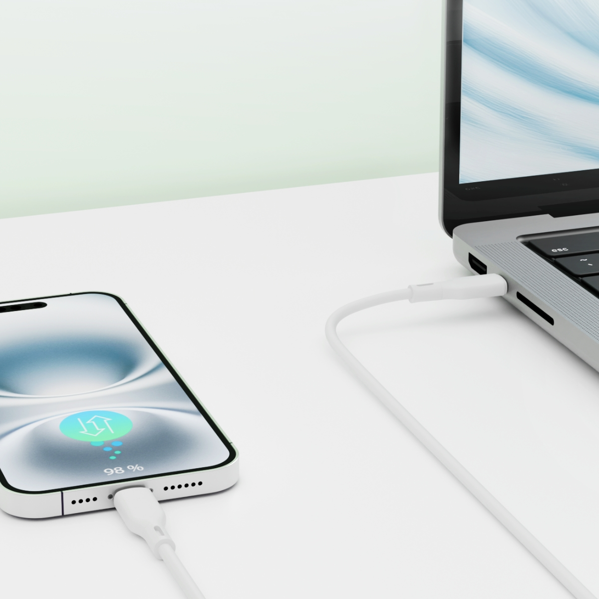 Telefon i laptop ładują się białym kablem. Telefon pokazuje symbol ładowania na poziomie 98%.