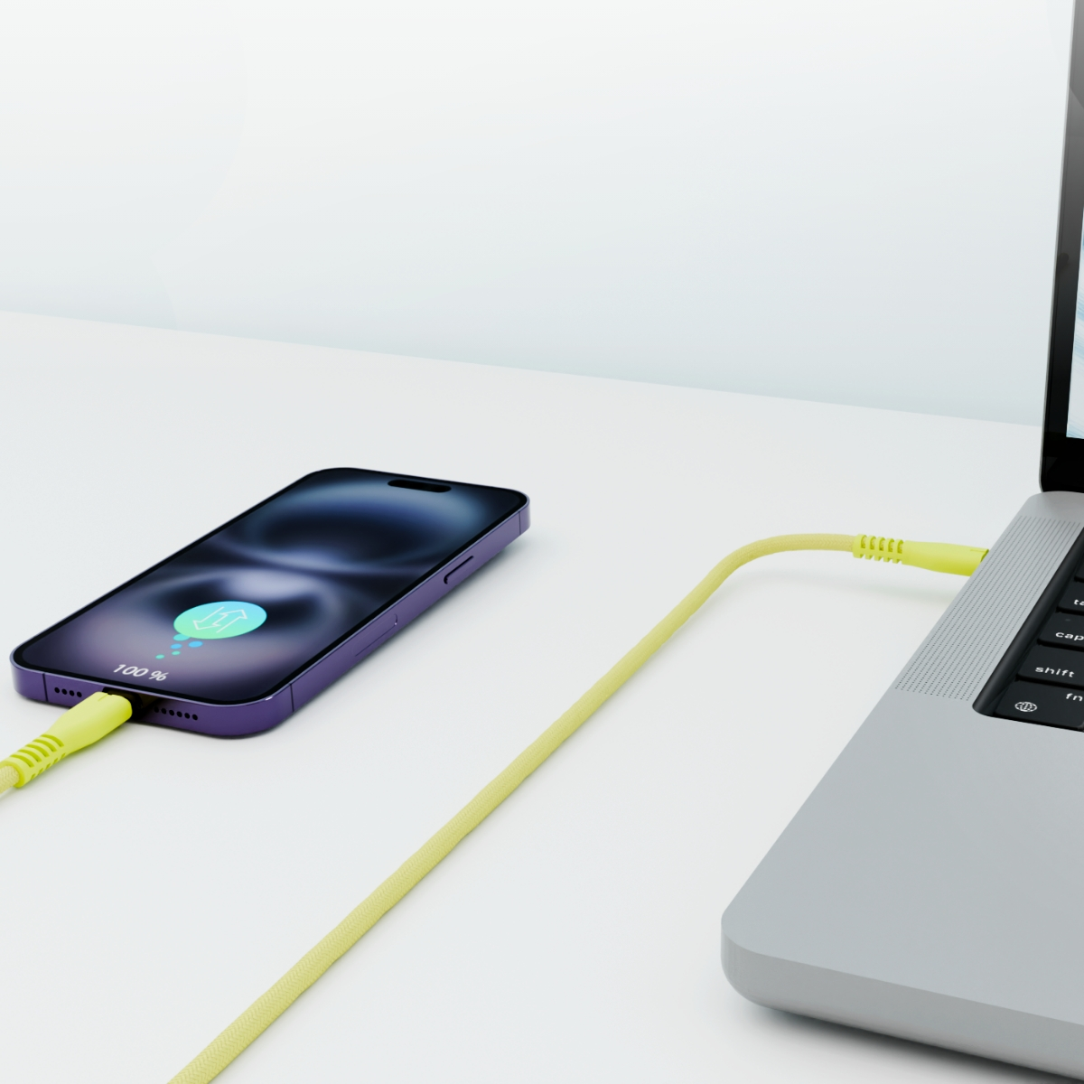 Telefon ładuje się z laptopa za pomocą żółtego kabla, na białym biurku.