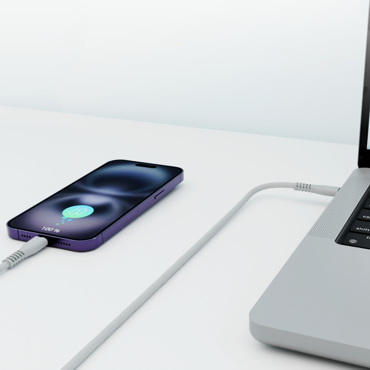 Fioletowy telefon ładujący się z laptopa szarym kablem na białej powierzchni. Telefon pokazuje 100% naładowania.