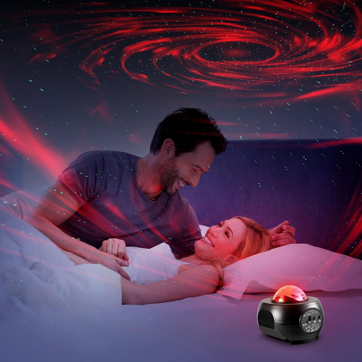 Ein Paar im Bett, beleuchtet von einem Galaxie-Projektor. Der Mann lächelt.