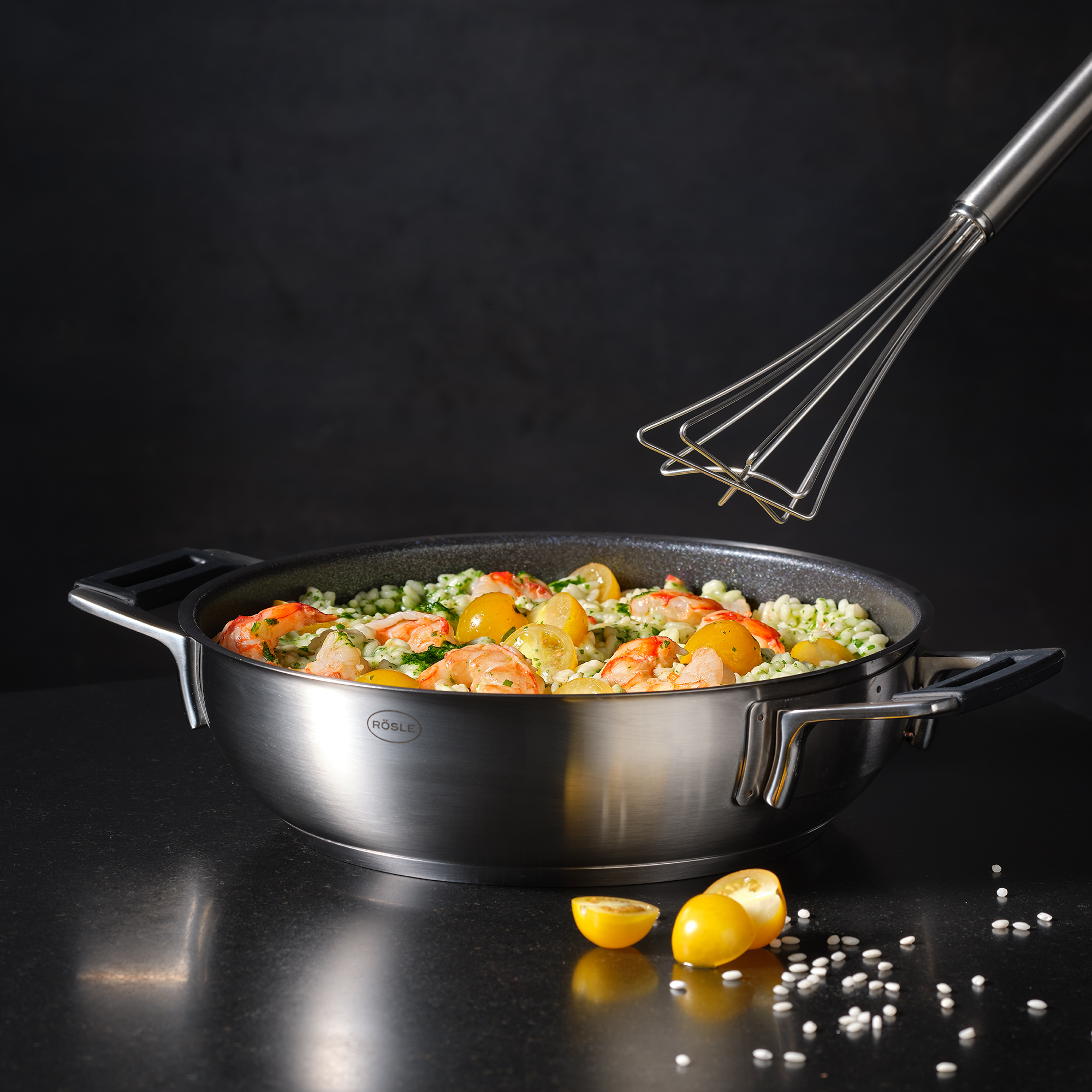 Topf mit Essen und Schneebesen. Gelbe Tomaten im Topf. Dunkle Oberfläche.