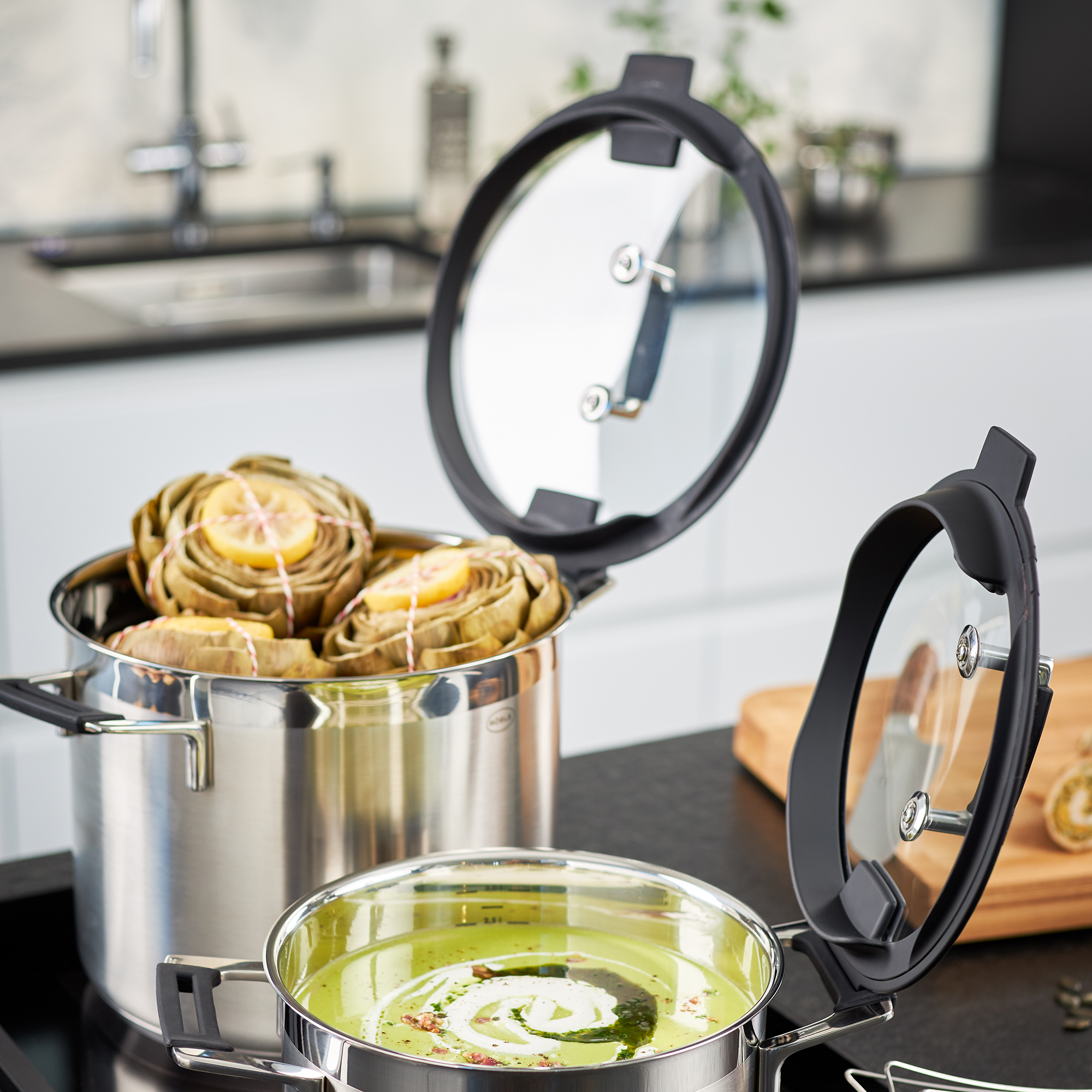 Casseroles en inox avec couvercles, une avec artichauts, l'autre avec soupe. Arrière-plan de cuisine.