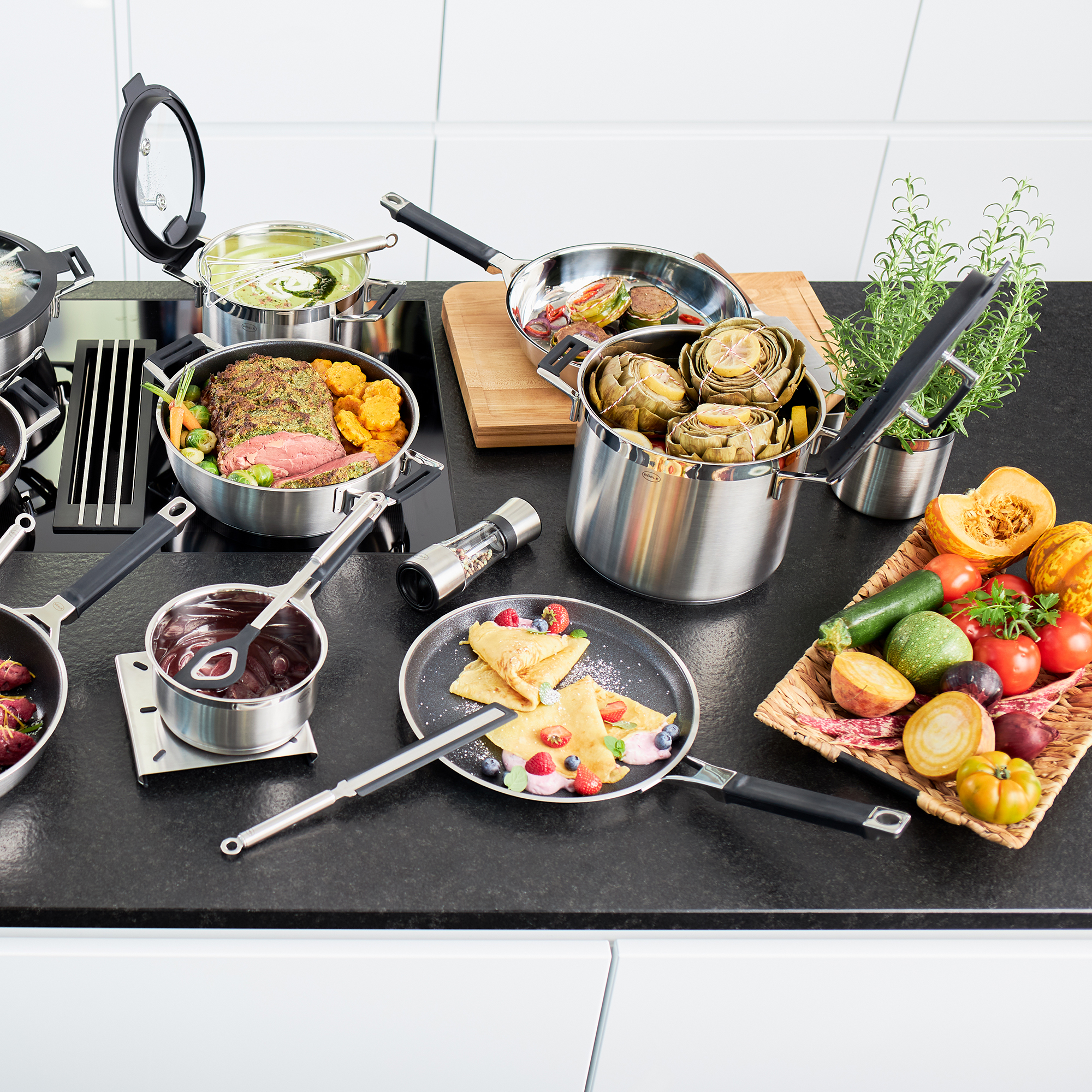 Configuration de cuisine avec des poêles, de la nourriture et des légumes. Divers éléments sur un comptoir noir.