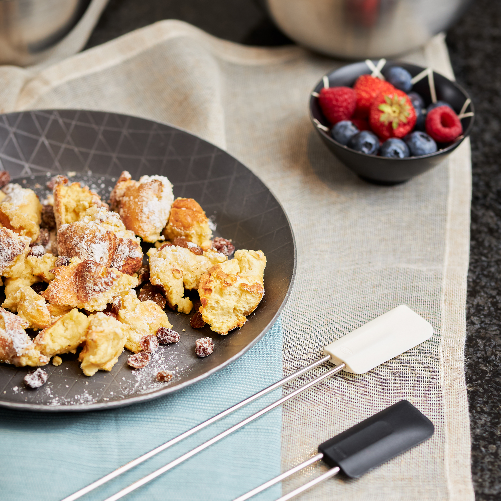 Nahaufnahme eines Tellers mit Essen, Beeren und einer Schüssel. Spatel sind vorne.
