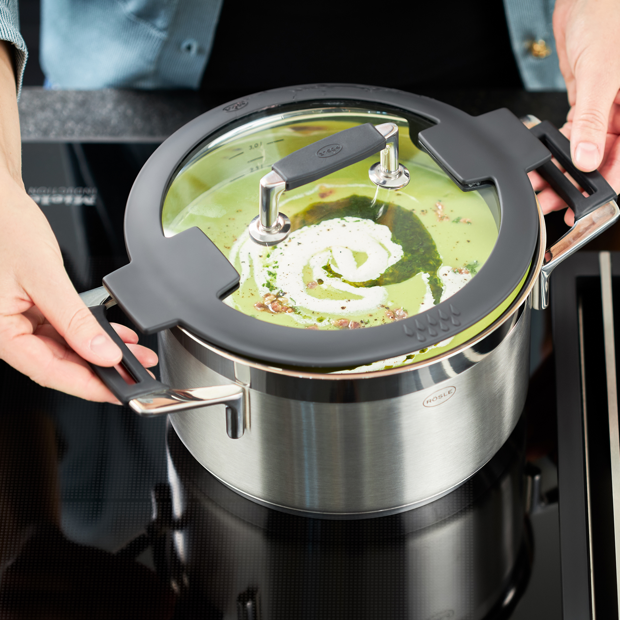 Mains tenant le couvercle d'une casserole avec de la soupe sur la cuisinière. Fond noir.