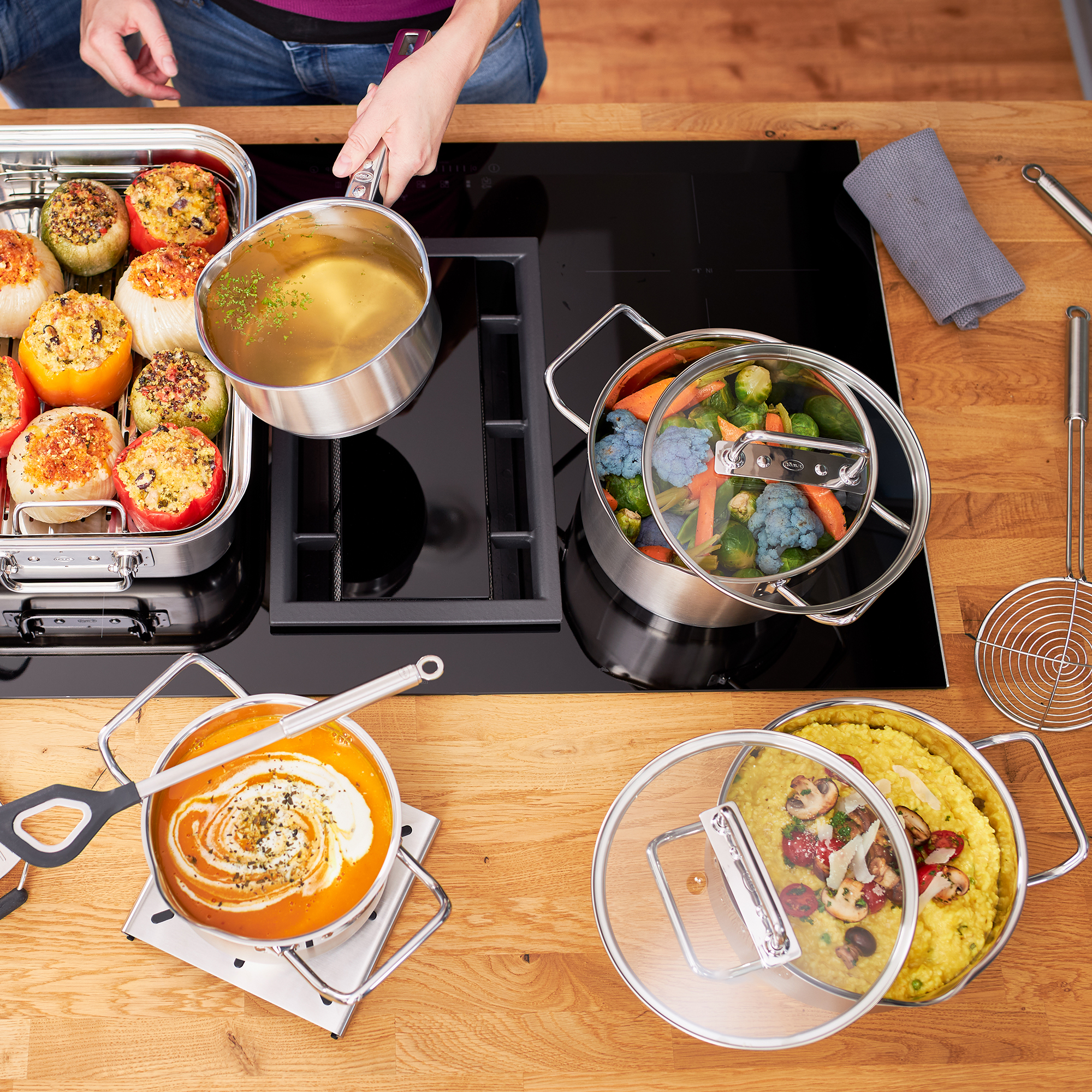 Vue de dessus d'un comptoir de cuisine en bois avec des casseroles, des poêles et divers aliments en préparation.
