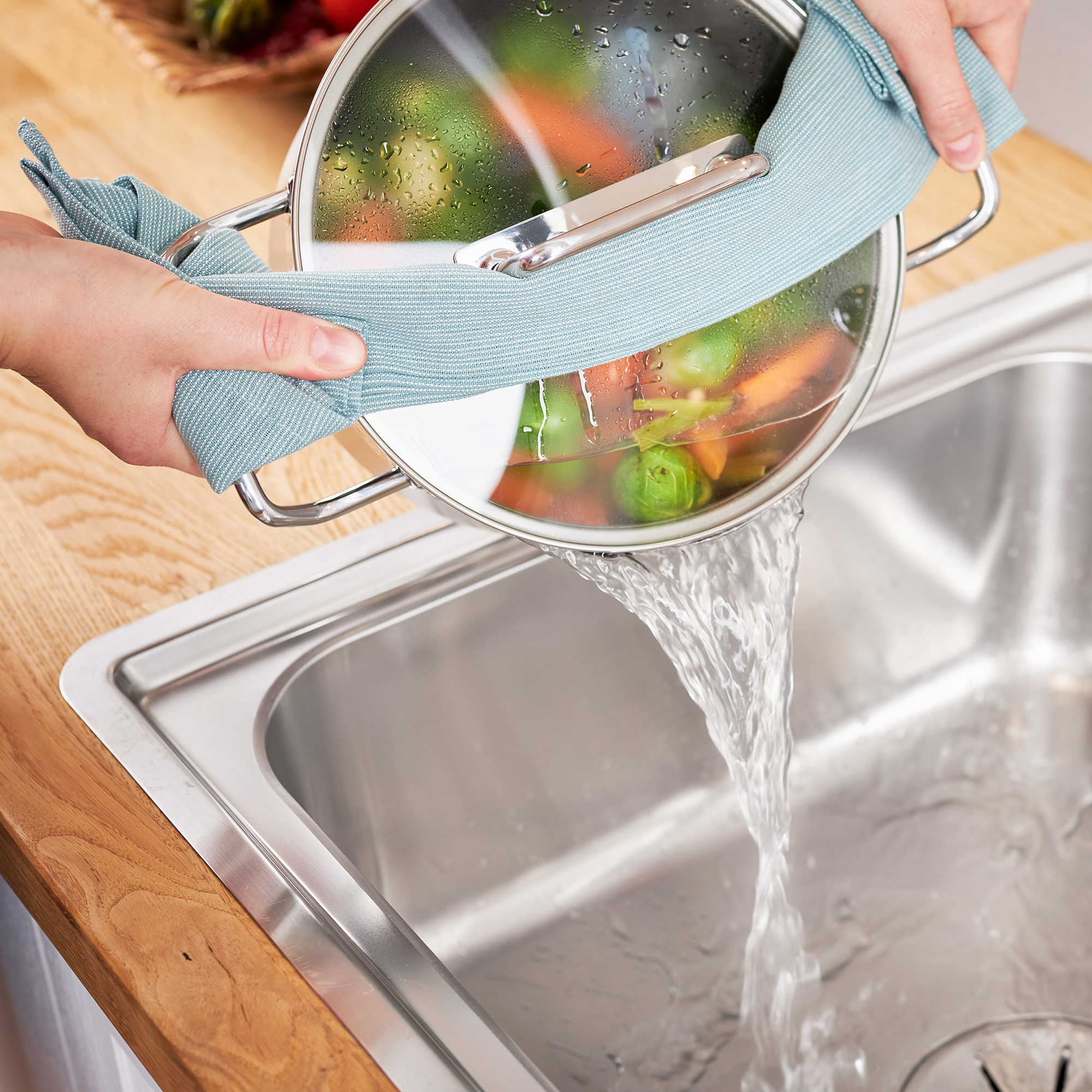 Mains versant de l'eau d'une casserole dans un évier. Légumes dans la casserole. Plan de travail en bois.