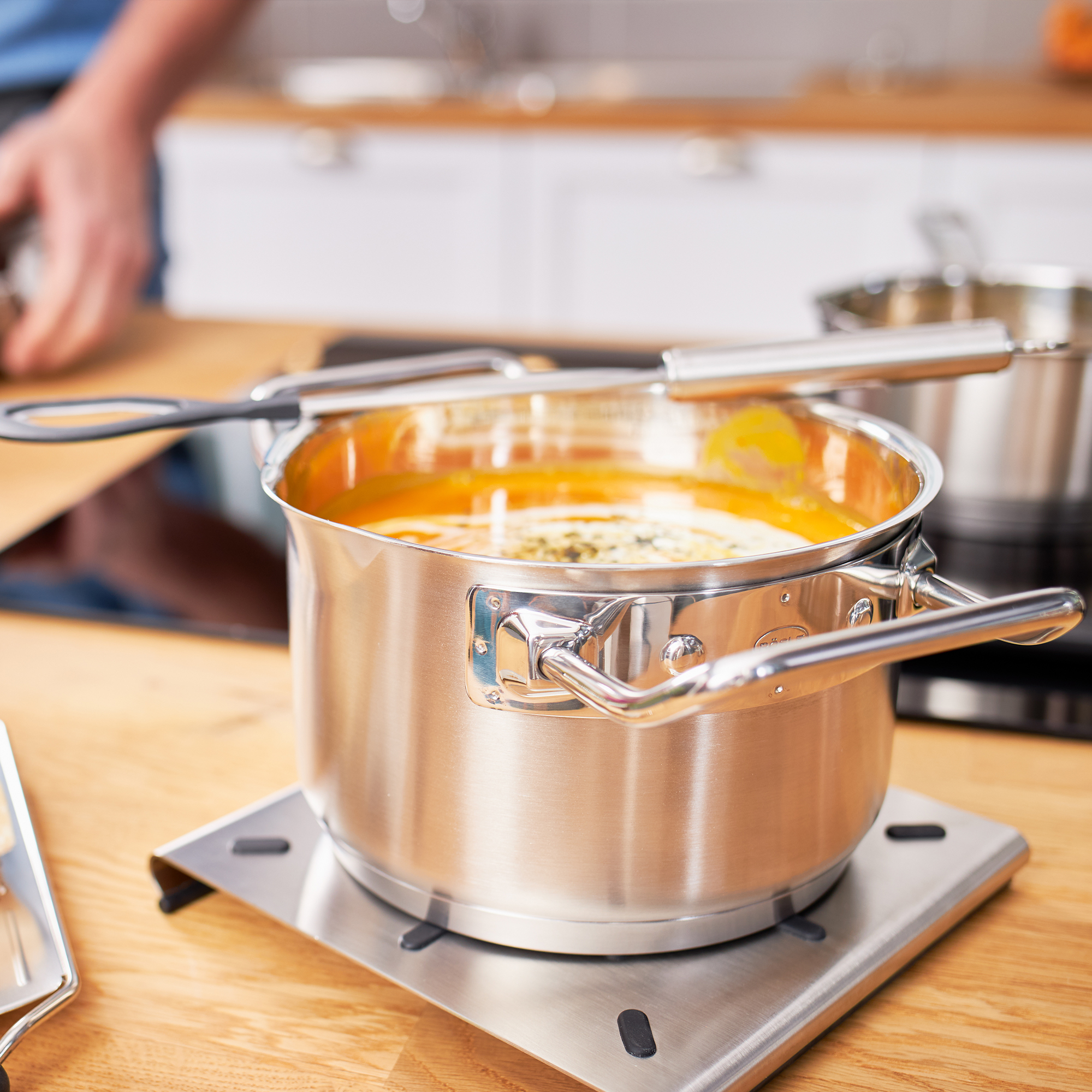Une casserole en acier inoxydable sur un brûleur, avec une soupe jaune à l'intérieur.