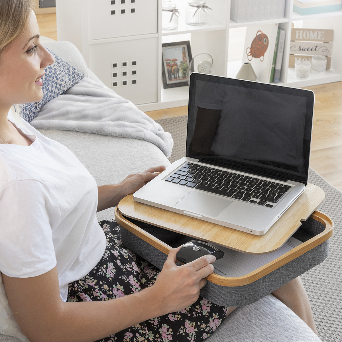 Eine Frau sitzt auf einem Sofa und benutzt einen Laptop auf einem Schoßtisch und hält eine Maus.