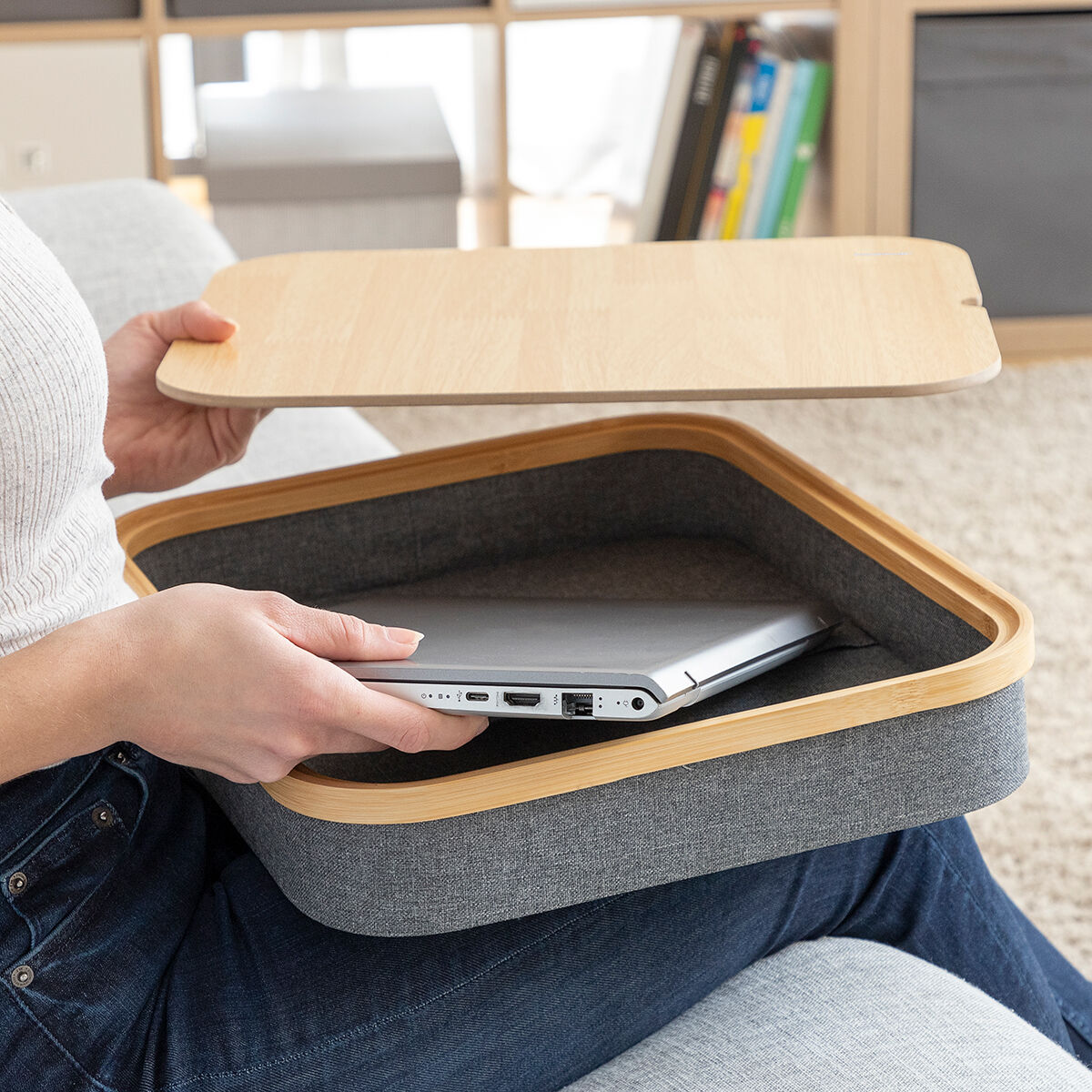 Eine Frau hält ein Holztablett mit Laptop, auf dem Schoß. Das Tablett hat grauen Rand.