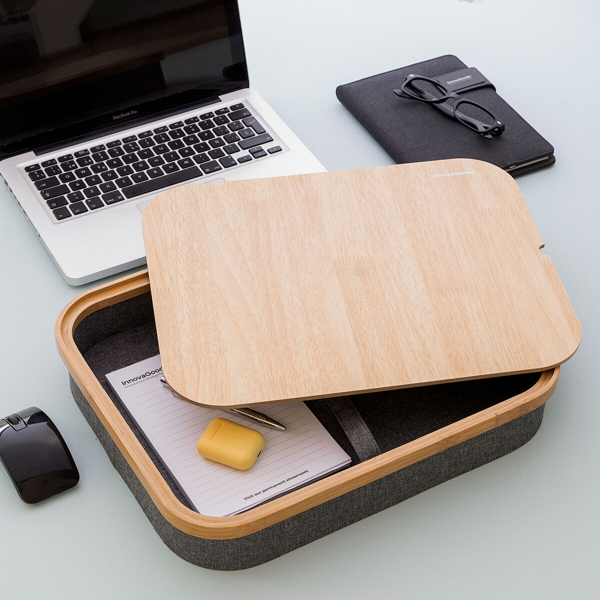 Ein Laptop auf einem Holztablett mit Zubehör, auf weißer Oberfläche. Das Tablett hat einen grauen Rand.