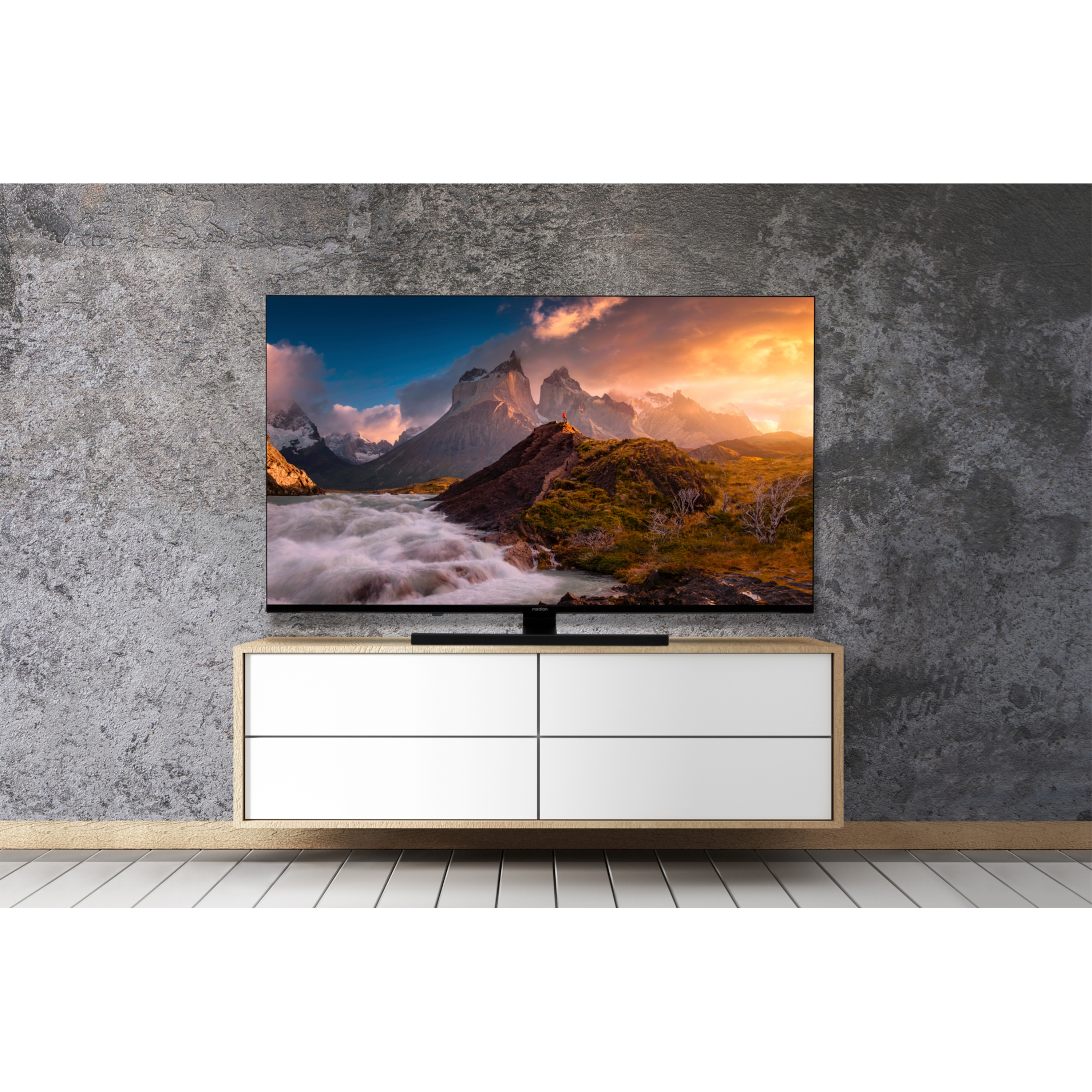 Moderner Fernseher auf weißem Schrank. Berglandschaft auf dem Bildschirm. Graue Wand. Weißer Boden.