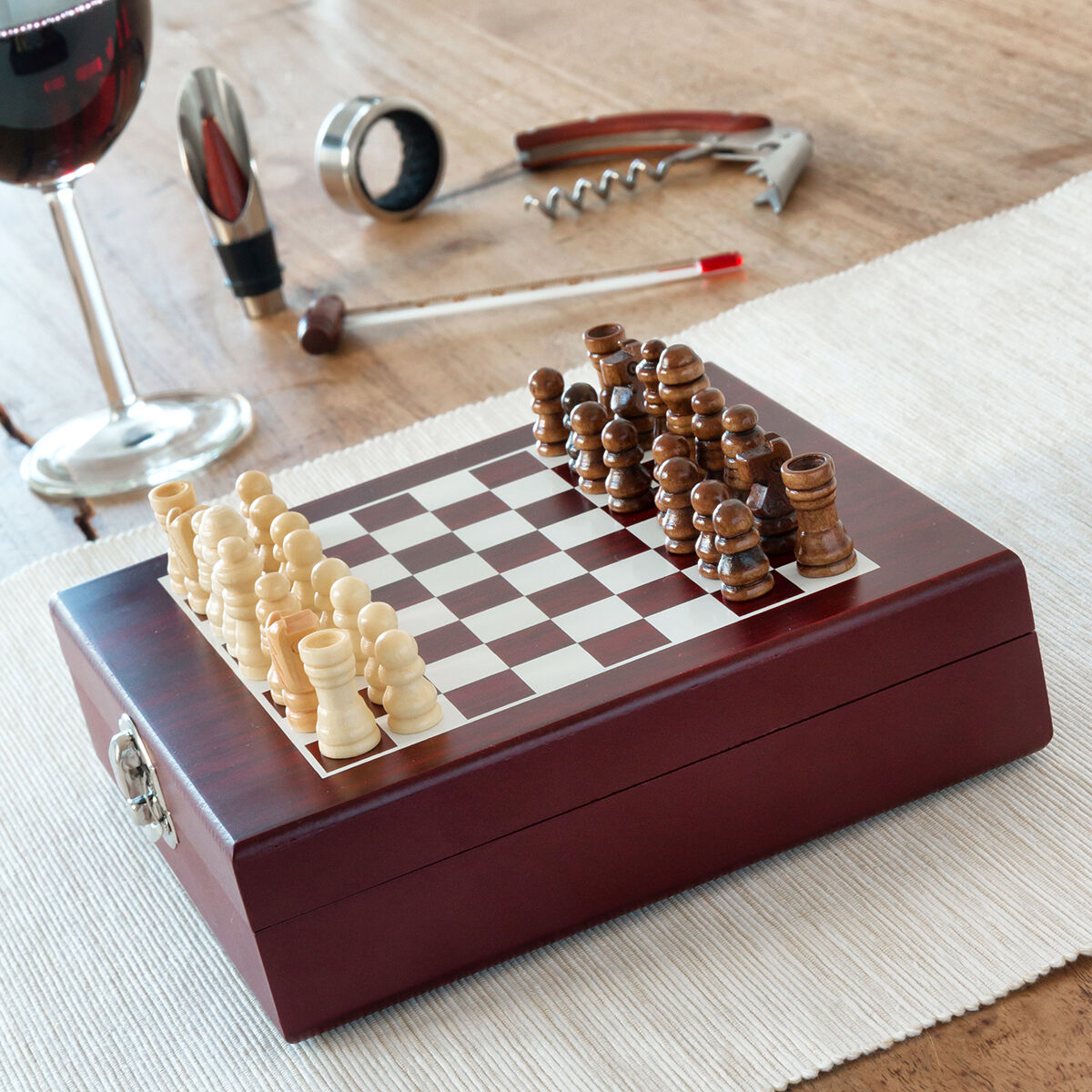 Juego de ajedrez sobre una mesa con copa de vino y accesorios. Tablero con piezas, blancas y marrones.