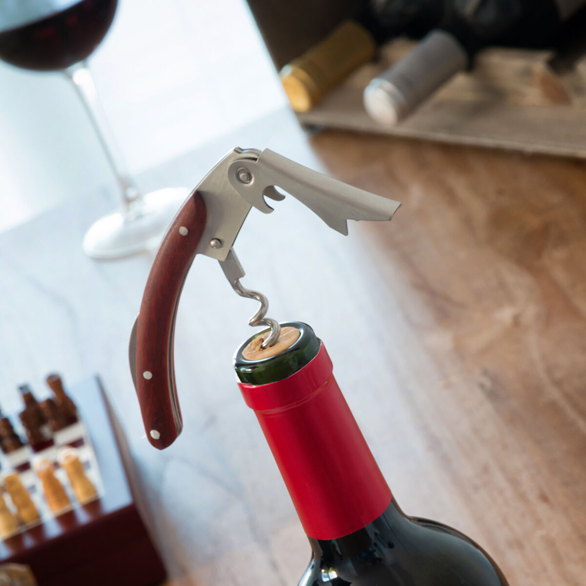 Una botella de vino con un sacacorchos. Una copa de vino en el fondo. Mesa de madera.