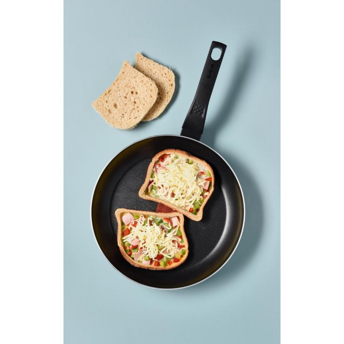 Frying pan with two toast slices topped with cheese, ham, and veggies. Blue background.