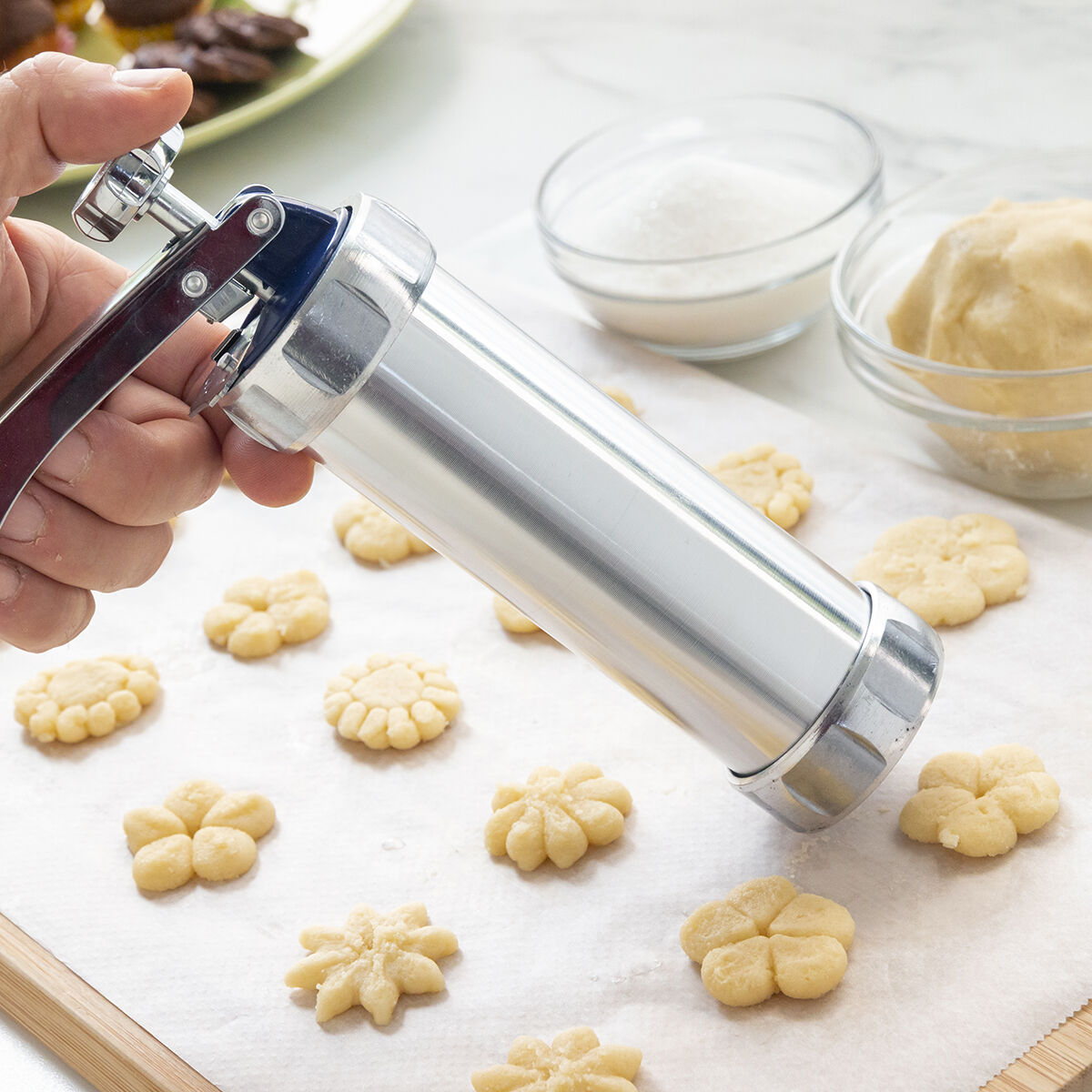 Pressa per biscotti con biscotti e ingredienti. Una mano preme una pressa per biscotti.