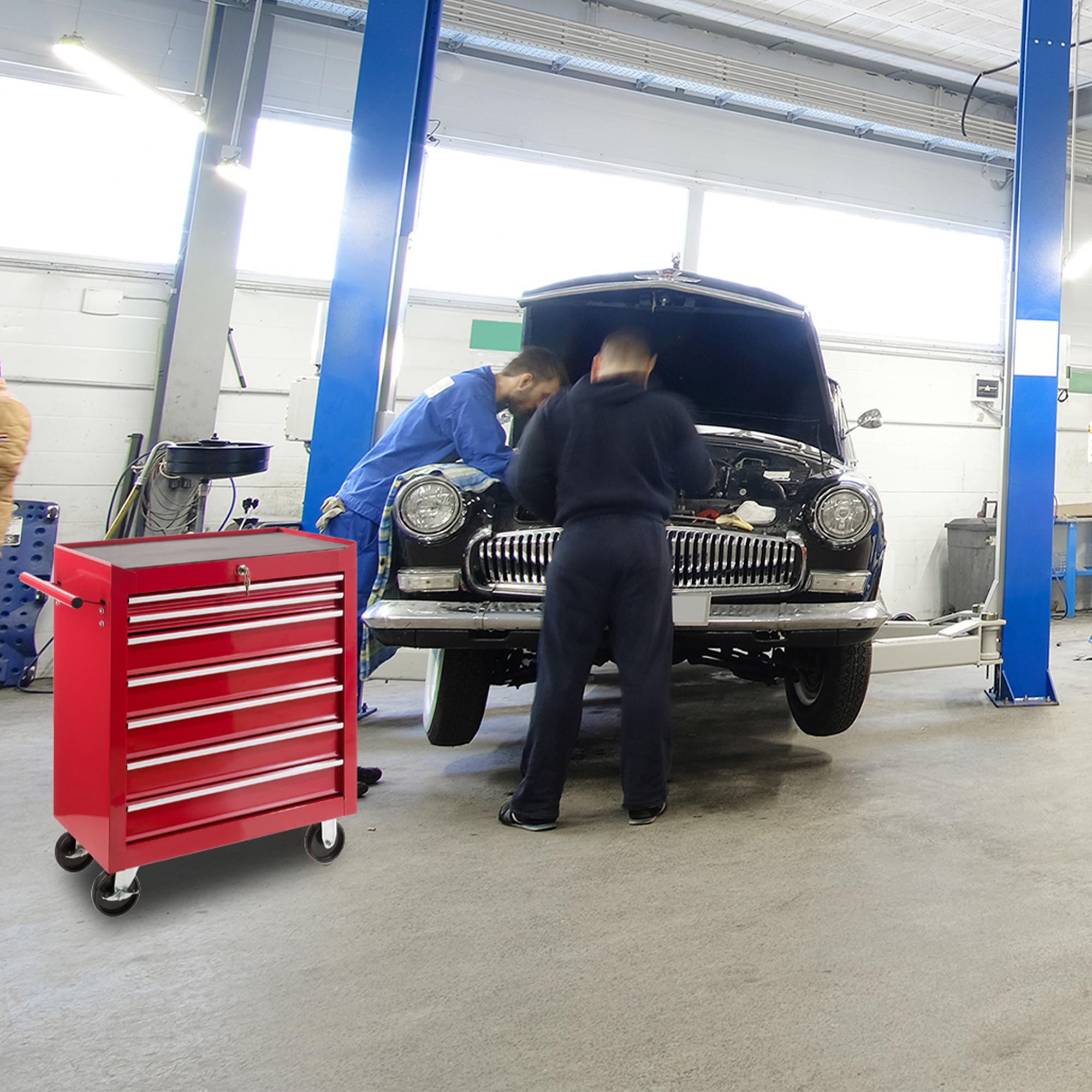 Zwei Mechaniker arbeiten in einer Garage an einem schwarzen Auto, mit roter Werkzeugkiste.