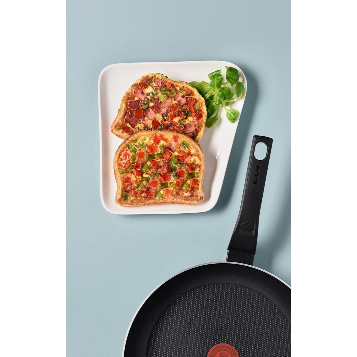 Two slices of toast with toppings. A pan in the foreground. Green garnish.