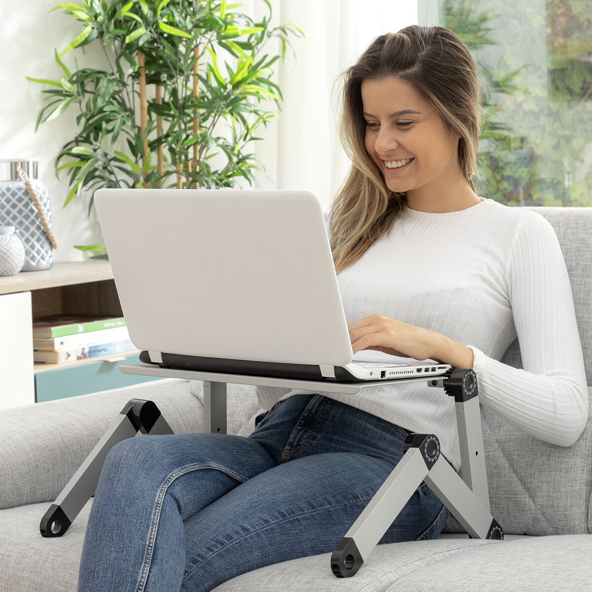 Donna che usa un laptop su un supporto per laptop mentre è seduta su un divano grigio.