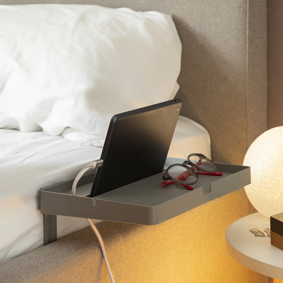 Tablet su un vassoio grigio, occhiali e una lampada.