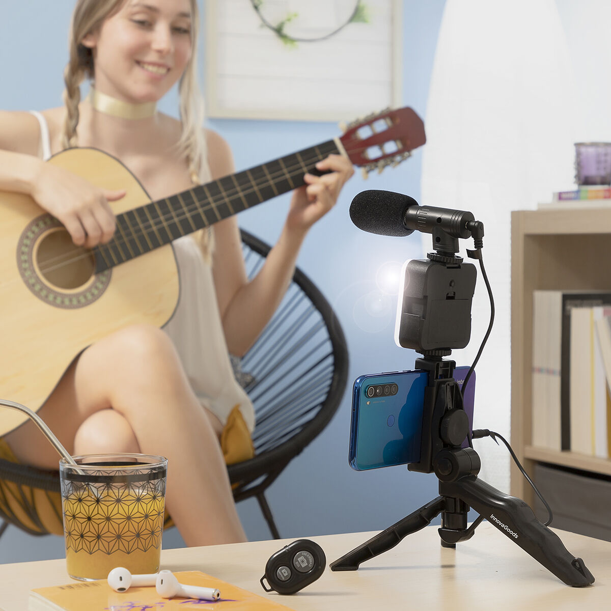 Mujer tocando guitarra, teléfono en trípode, vaso con bebida y pajita.
