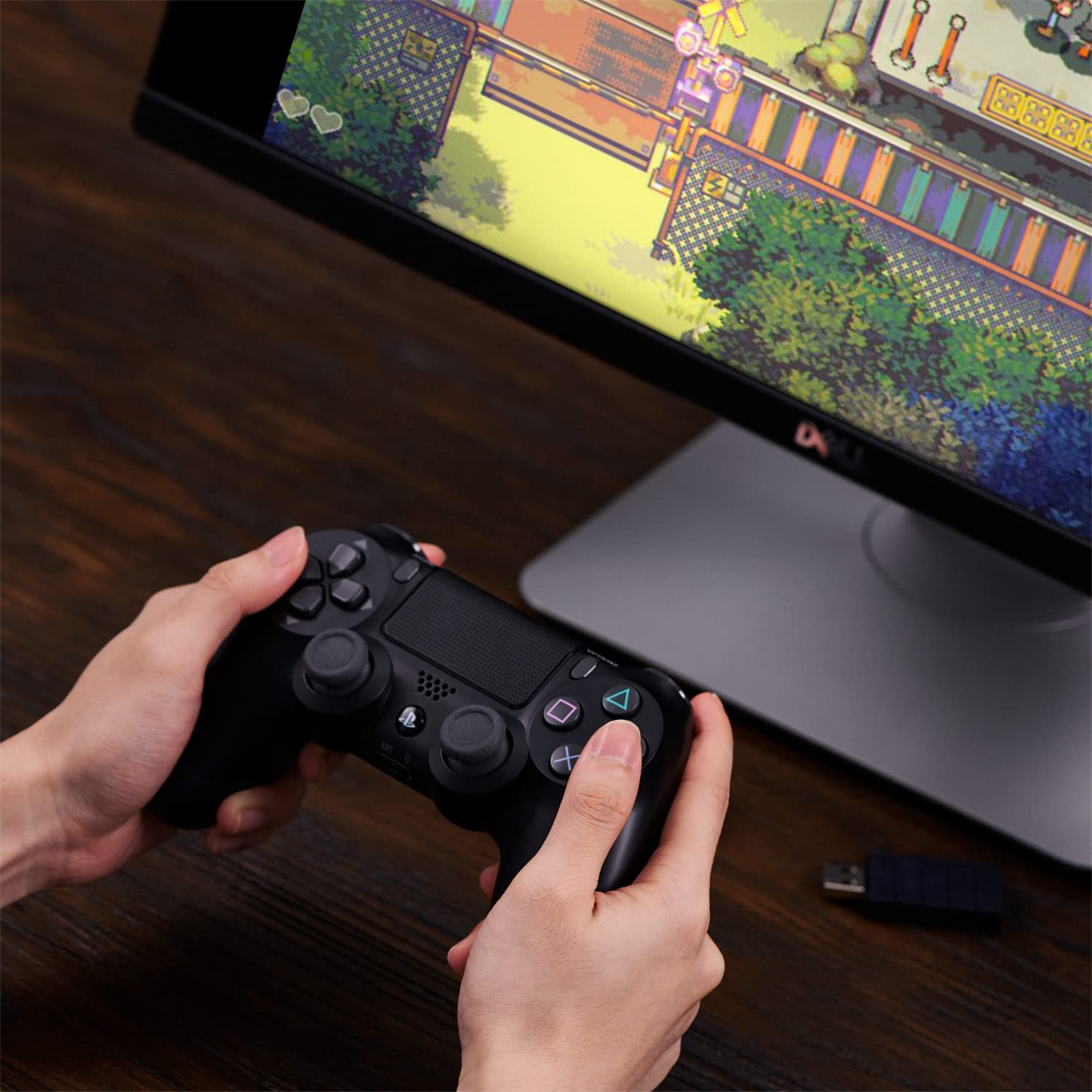Hände halten einen schwarzen Gamecontroller vor einem Monitor, der ein Spiel zeigt.