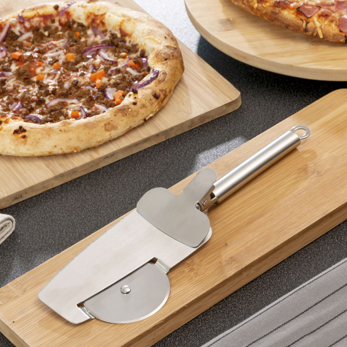 Un tagliapizza e una pizza su un tagliere di legno. C'è un'altra pizza sullo sfondo.
