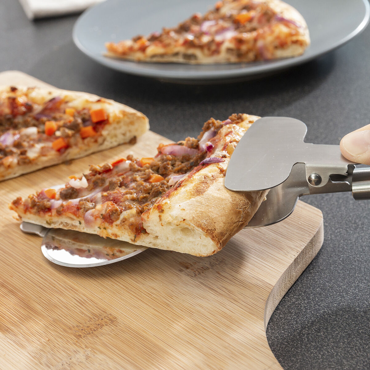 Fetta di pizza sollevata con un taglia pizza su un tagliere, un'altra fetta è su un piatto.