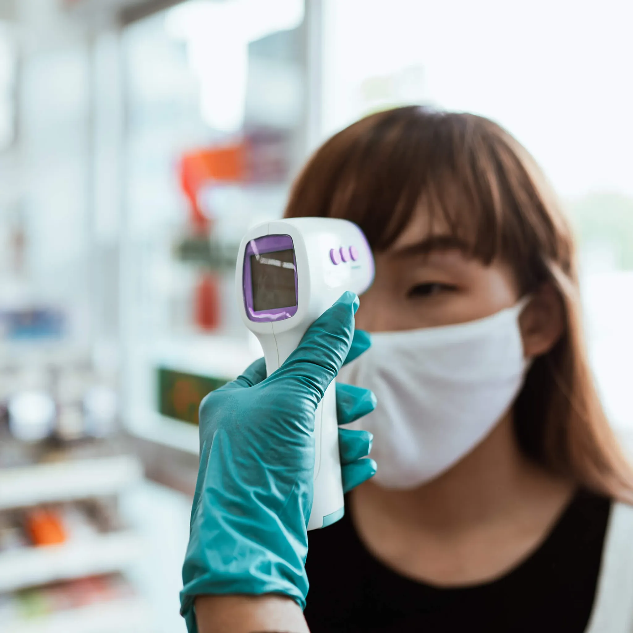 Eine Frau mit Maske lässt ihre Temperatur mit einem Thermometer messen. Sie ist in einem Geschäft.