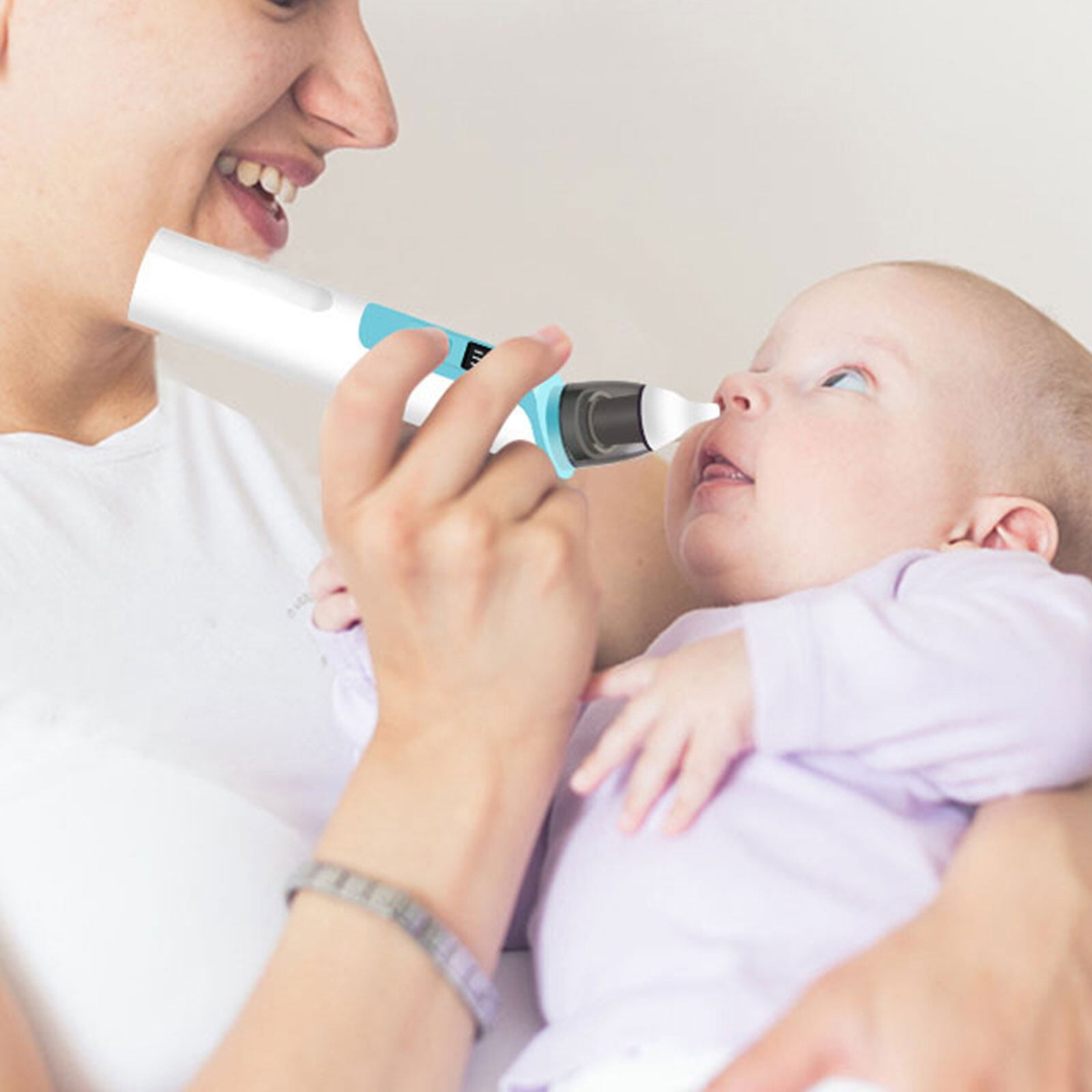 Eine Frau verwendet einen Nasensauger an einem Baby. Das Baby blickt nach oben, die Frau lächelt.
