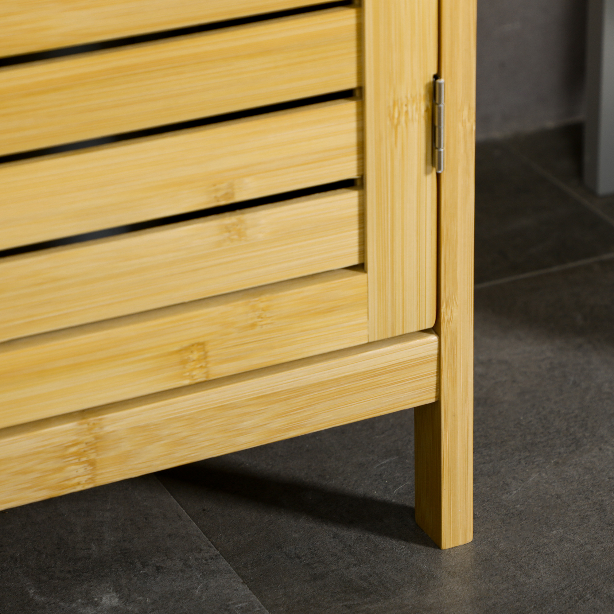 Nahaufnahme eines Holzschranks. Der Schrank hat eine Lamellentür und steht auf einem grauen Boden.