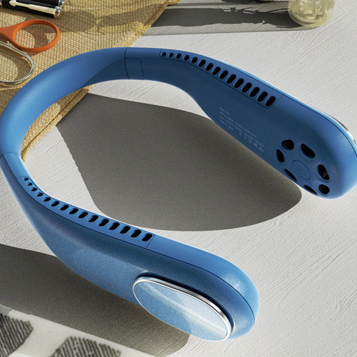 Blauer Nackenfächer auf grauer Oberfläche. Er hat ein geschwungenes Design mit Lüftungsschlitzen und einem Silberknopf.