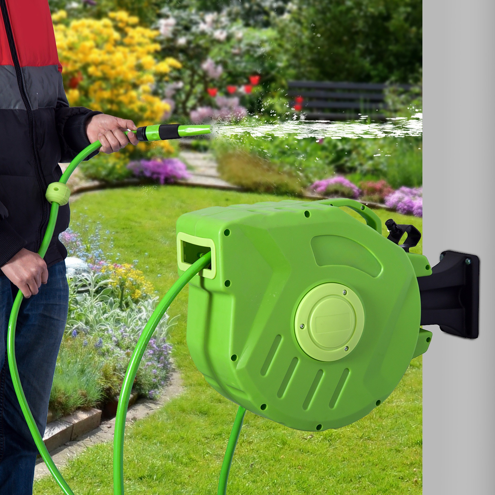 Eine Person bewässert einen Garten mit einem grünen Schlauch und einer grünen Schlauchtrommel an einer Wand.