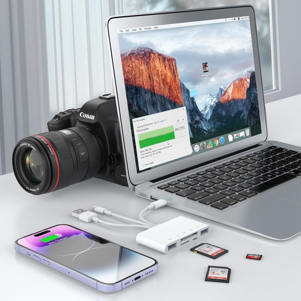 Laptop, Kamera, Telefon und Zubehör auf weißer Oberfläche angeordnet, was die Datenübertragung anzeigt.