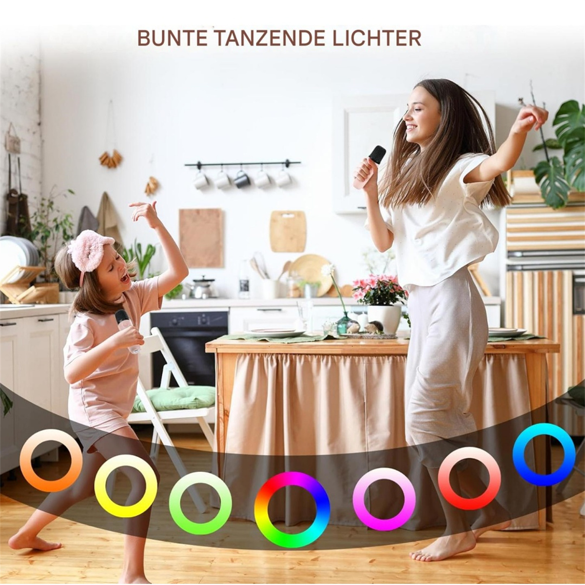 Zwei Frauen tanzen mit Mikrofonen in einer Küche, bunte Lichtringe unter ihnen.