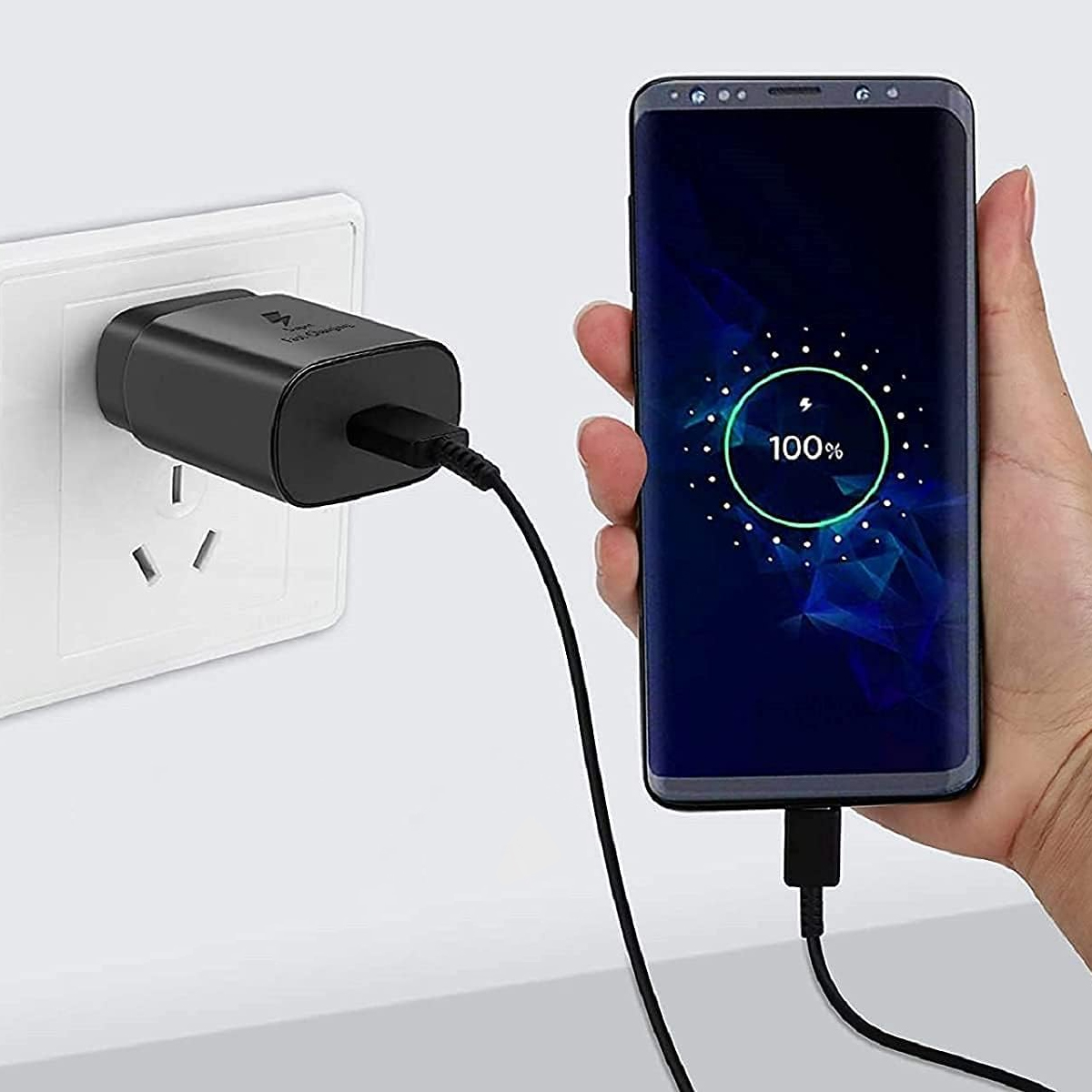 Schwarzes Ladegerät in einer Steckdose, lädt ein Telefon.