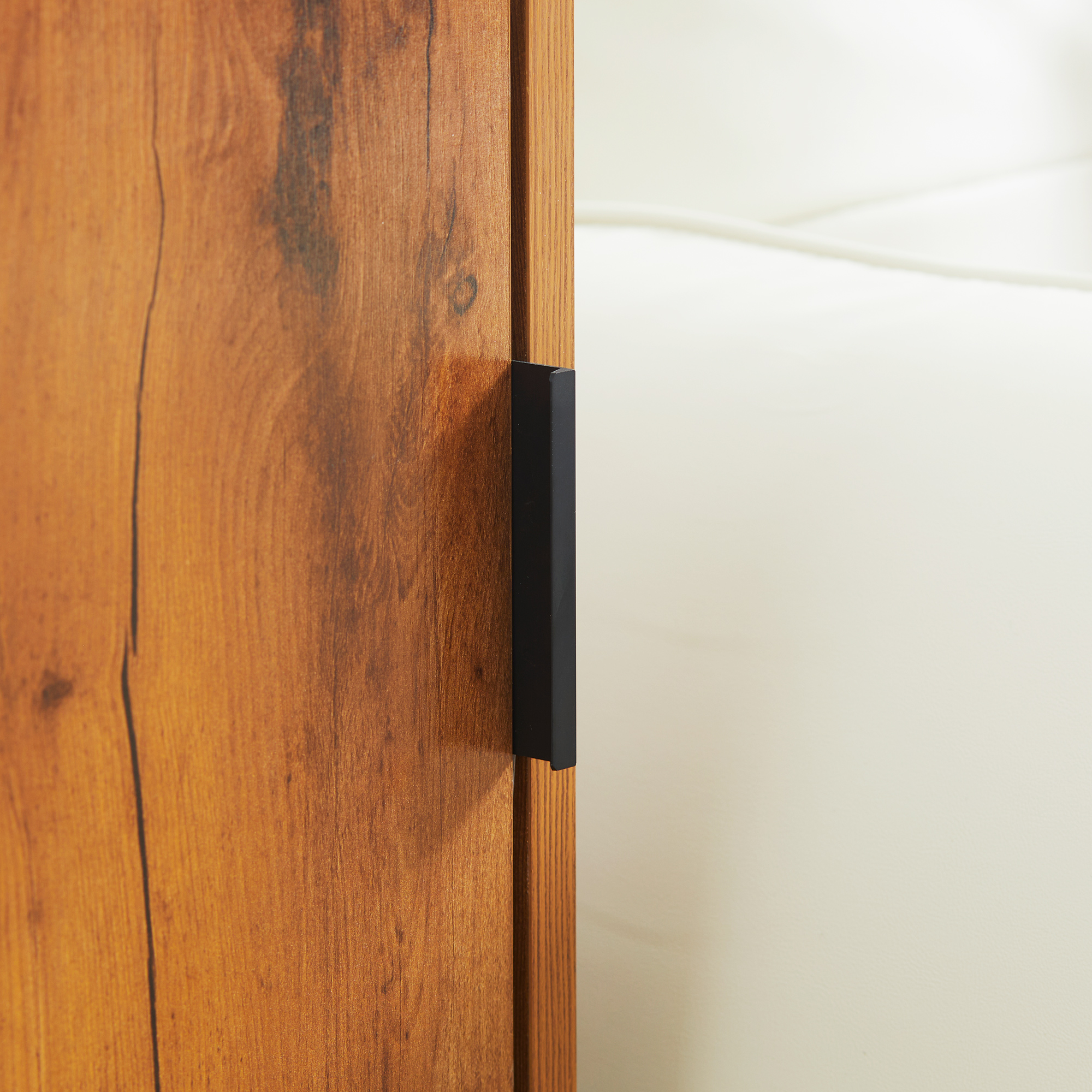 Nahaufnahme einer Holzschranktür mit schwarzem Griff. Der Hintergrund ist ein verschwommenes Off-White.