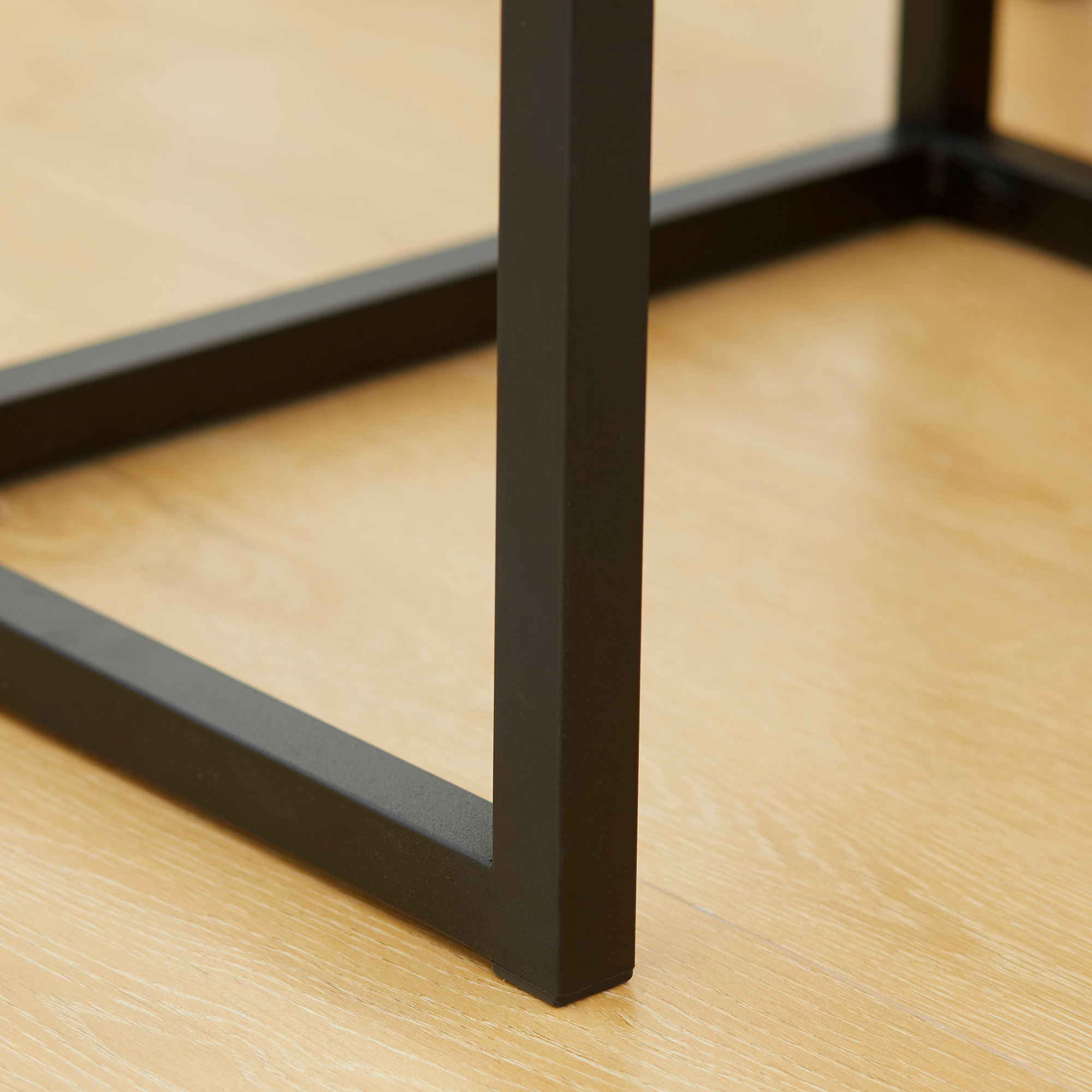 Nahaufnahme eines schwarzen Metall-Tischbeins, mit hellem Holzboden im Hintergrund.