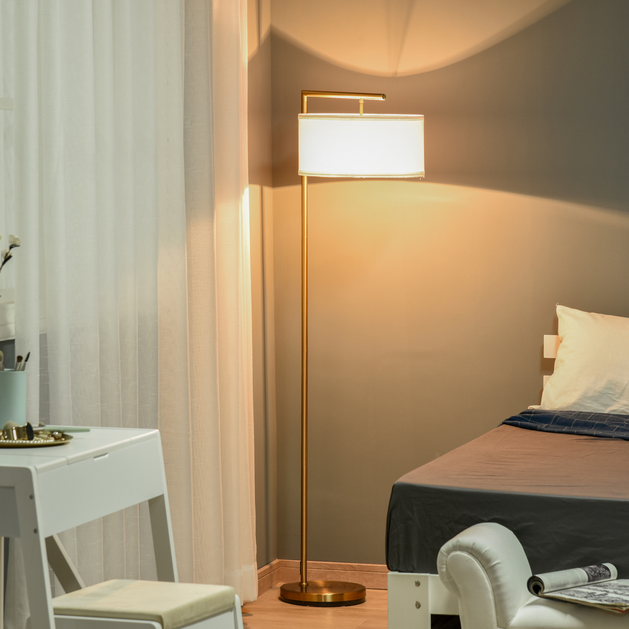 Eine goldene Stehlampe neben einem Bett. Sie scheint Licht auf eine graue Wand. Ein weißer Schreibtisch und Vorhänge sind ebenfalls sichtbar.