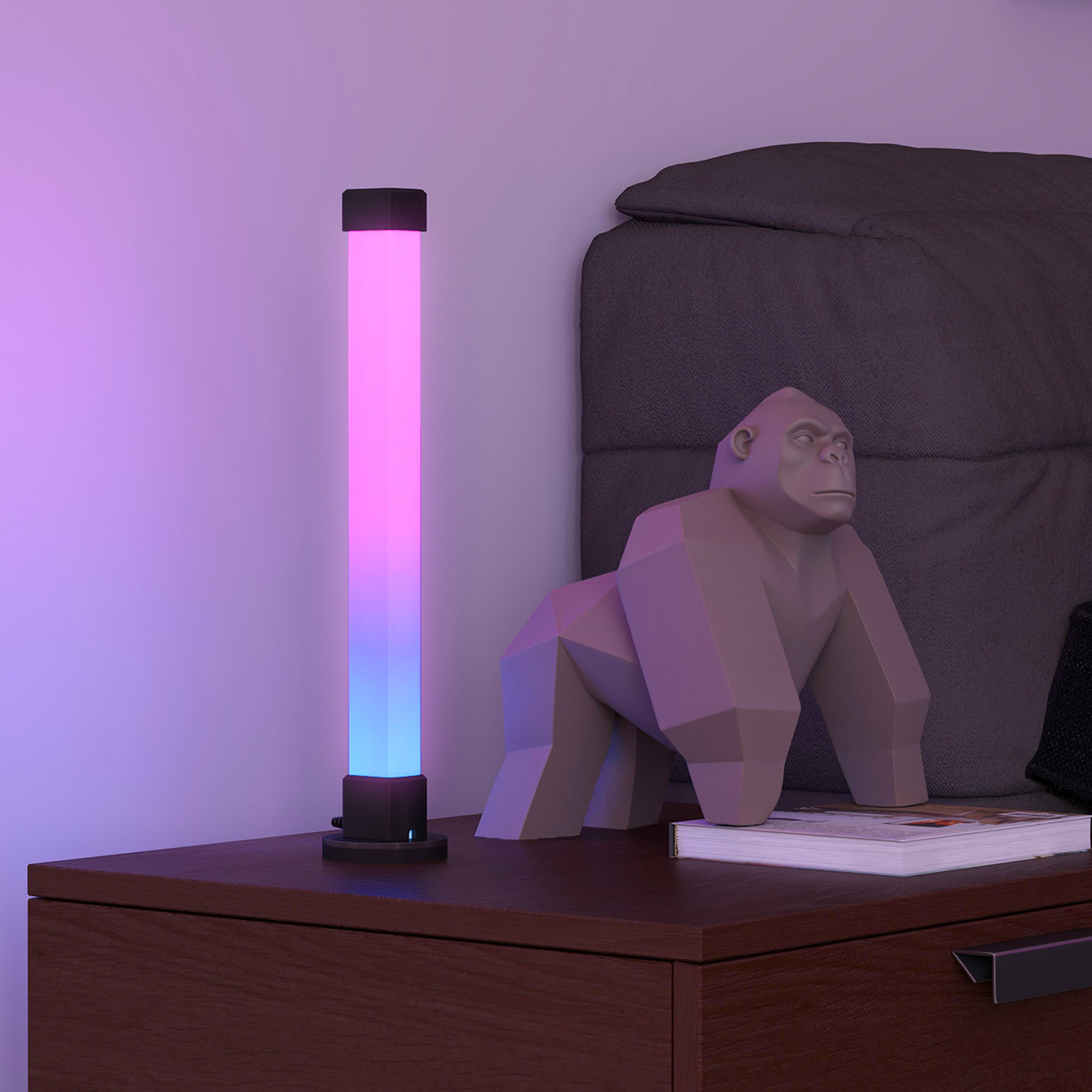 Beleuchtete Lampe neben Gorillastatue und Bett. Rosa, blaue und violette Farben. Schwarzer Sockel und Holzoberfläche.