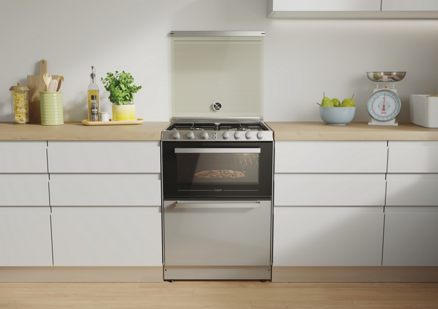 Un forno Candy con la parte superiore aperta. Ambiente cucina con bilancia e verdure sullo sfondo.