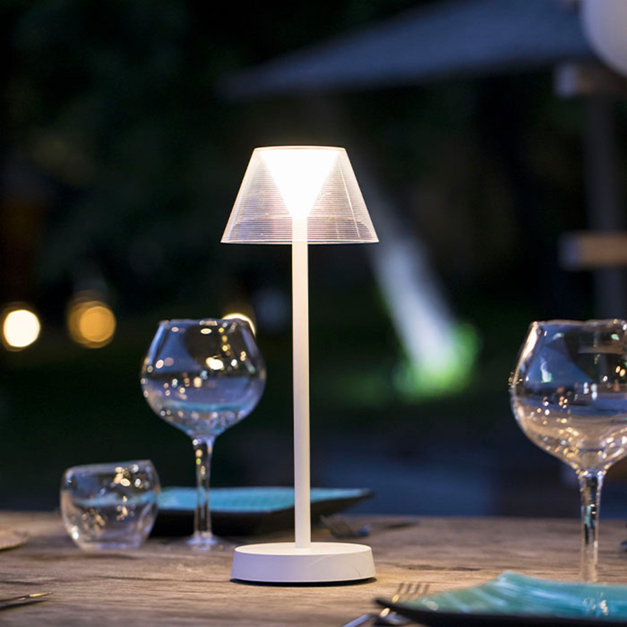 Tisch mit Gläsern und einer weißen Lampe mit durchscheinendem Lampenschirm. Der Hintergrund ist unscharf.