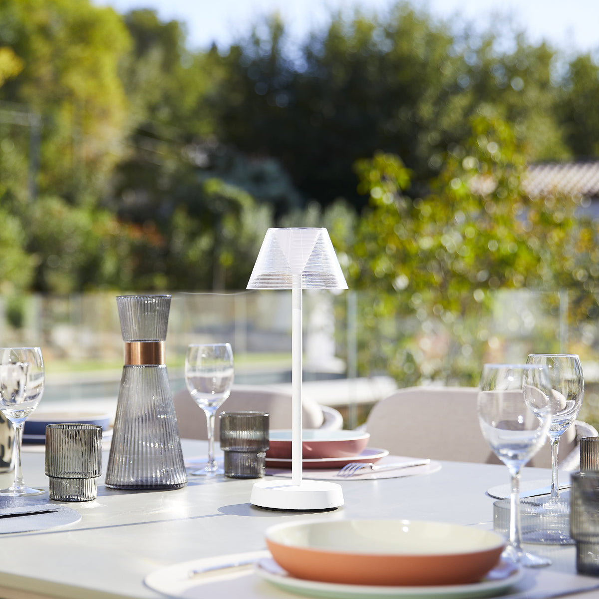 Outdoor-Esstisch-Arrangement. Tisch mit Lampe, Gläsern, Tellern und Essen. Grüner Hintergrund.
