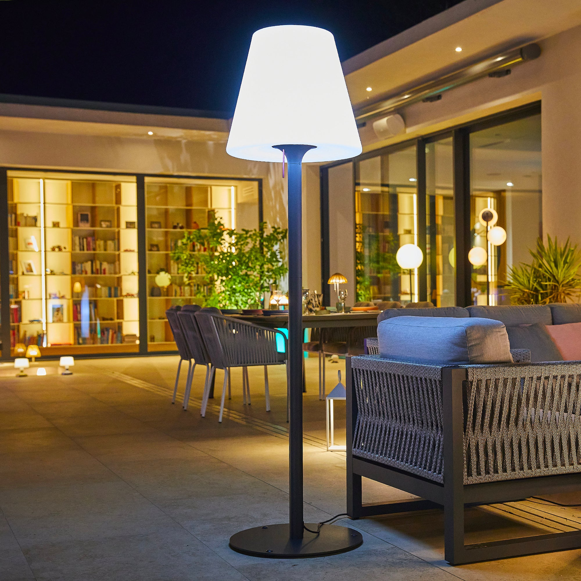 Lampada da terra per esterni. Palo alto e nero con paralume bianco. Ambiente diurno all'aperto.